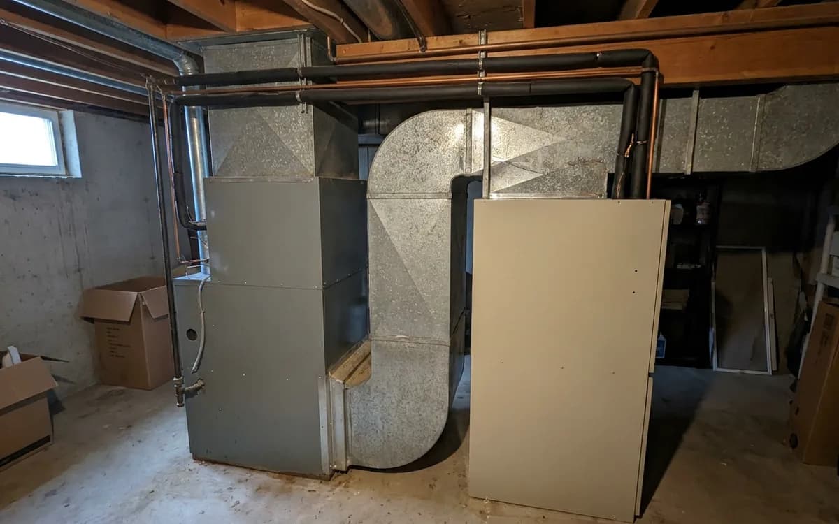 Basement furnace with metal ductwork beside a newly installed indoor air handler and copper refrigerant lines